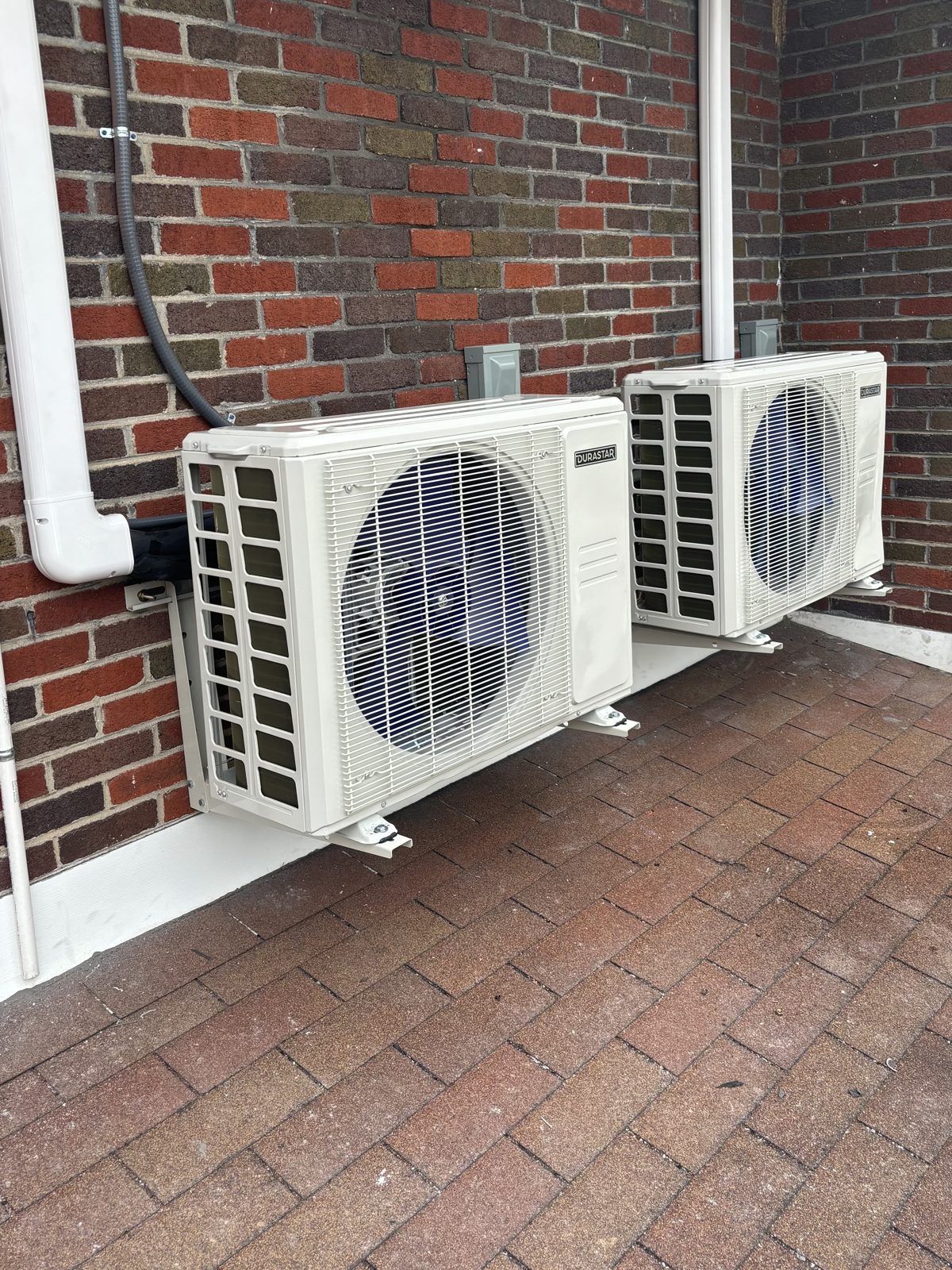 Two ductless mini-split outdoor condenser units mounted on a brick wall